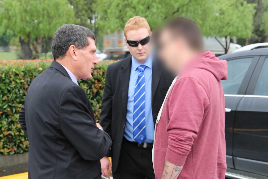 Two detectives speak to a man in a car park