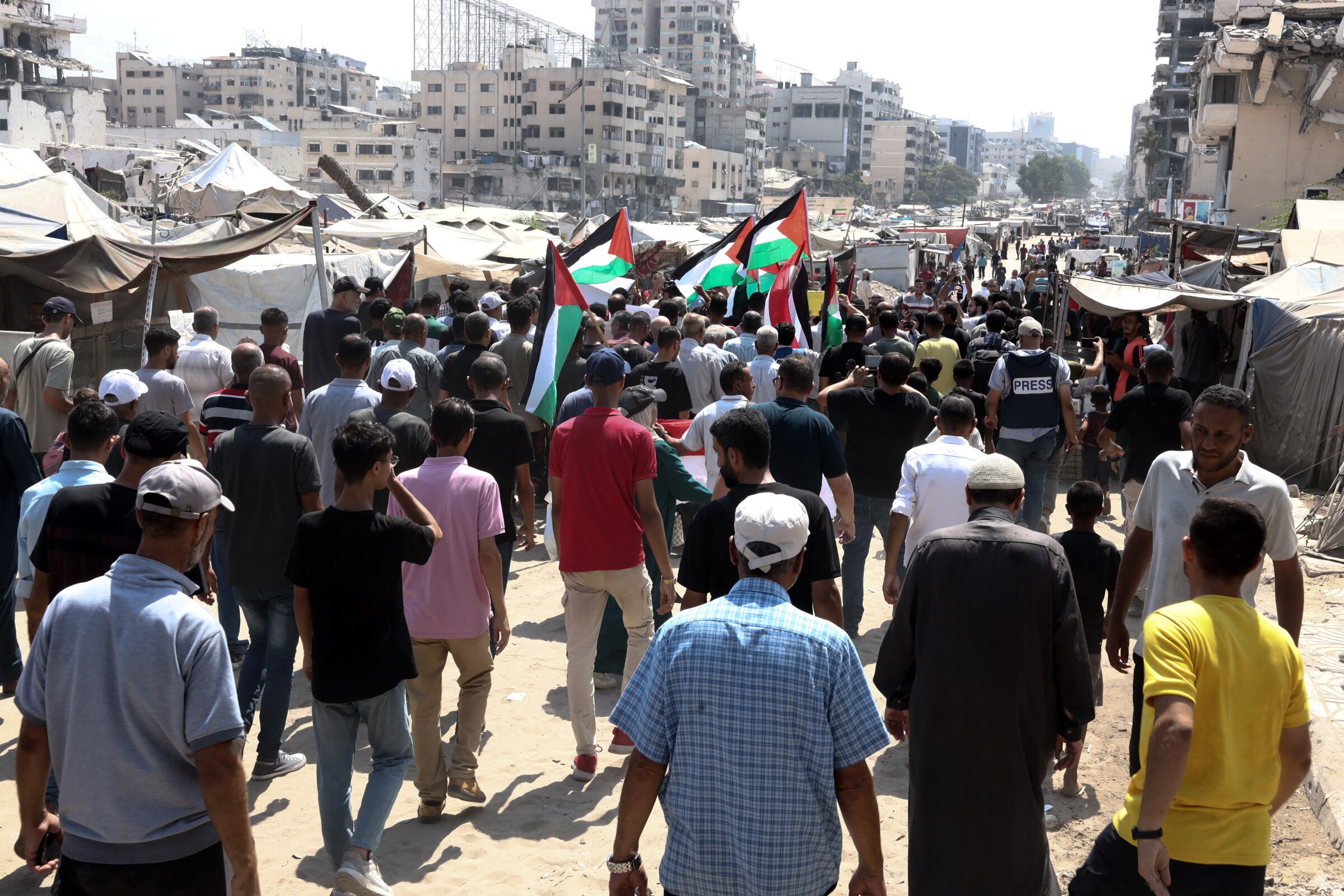 A large crowd seen from the back, with Palestinian flags visible.