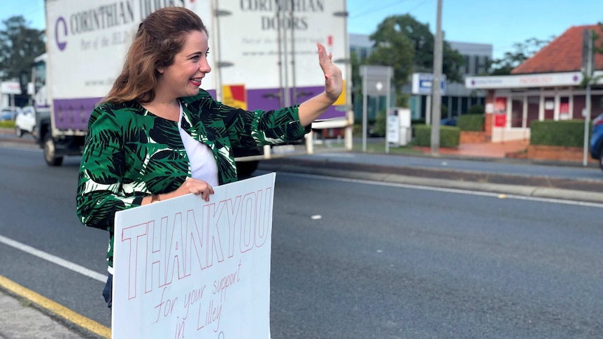 Anika Wells waves at cars while holding a sign that says "Thank you for your support in Lilley"