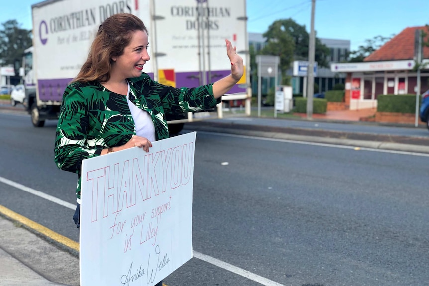 Anika Wells waves at cars while holding a sign that says "Thank you for your support in Lilley"
