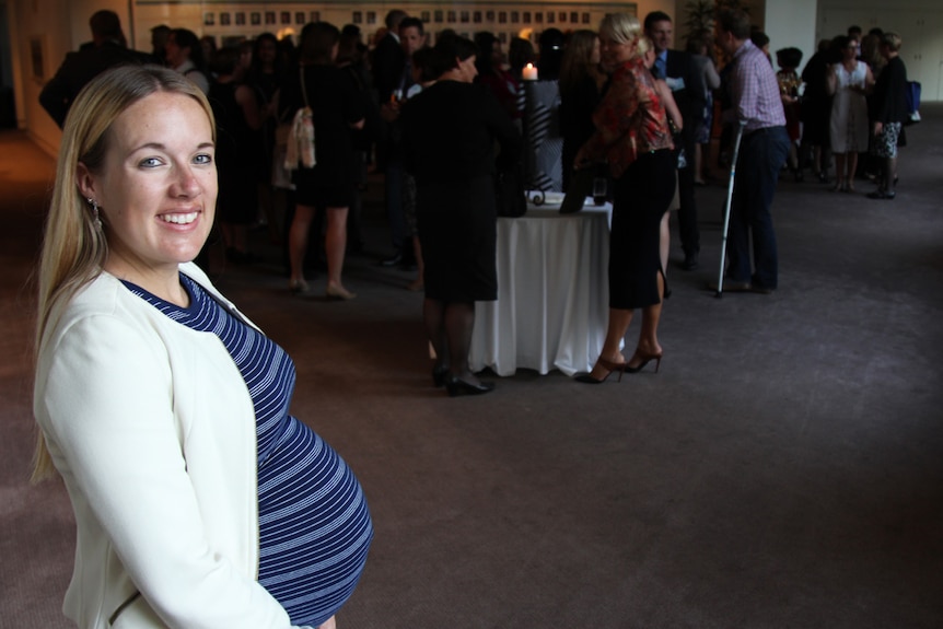 Pregnant lady smiling among crowd of people.