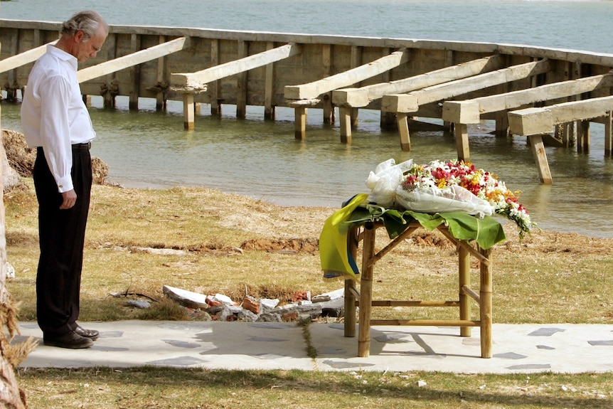 A man with his head bowed, looking at some flowers