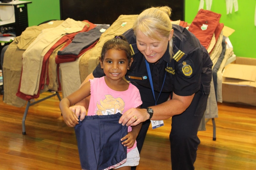A small girl with dark skin receives a pair of shorts from a woman in an Australian Border Force shirt.