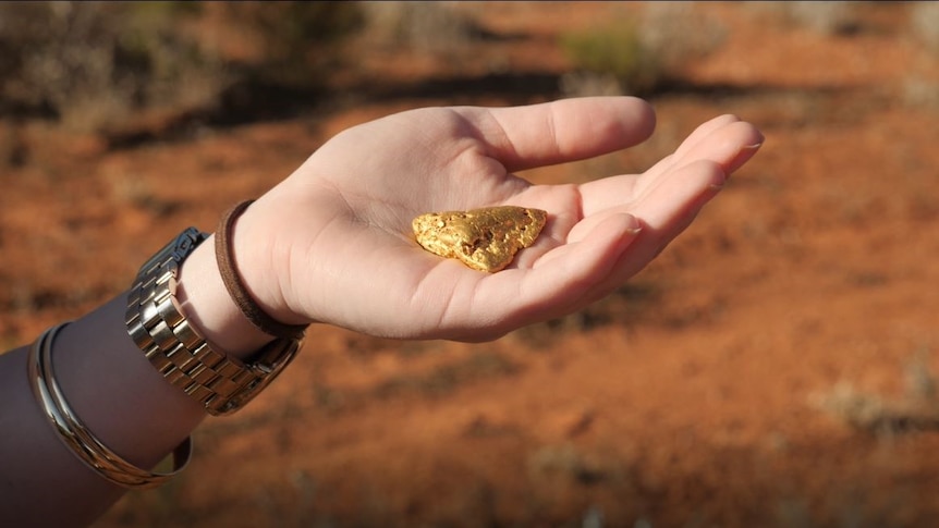 A woman holding a gold nugget in her hand.