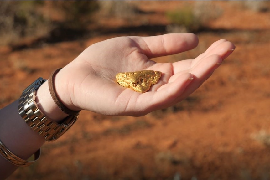 A woman holding a gold nugget in her hand.