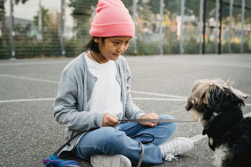 Boy wearing pink beanie sits with dog on concrete