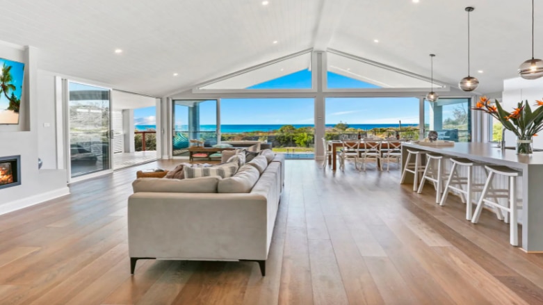 A large open air room with wood floors, a cream lounge and breakfast bench leads to ocean views.