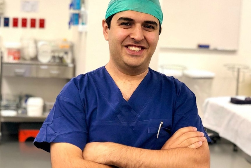 A man in blue scrubs smiles in an operating theatre.