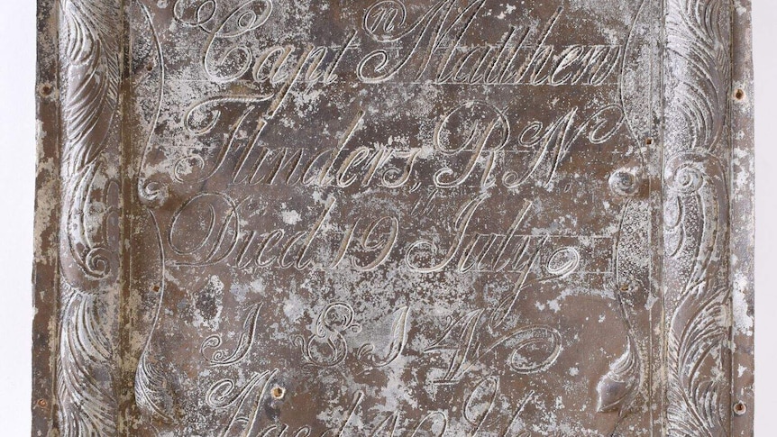 Brass breastplate is seen with cursive writing reading "Capt Matthew Flinders RW died 19 July aged 40 years".