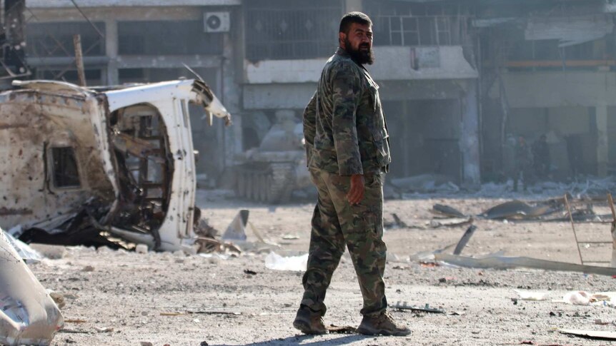 A Syrian pro-regime fighter walks in a bombed-out street in Ramousah