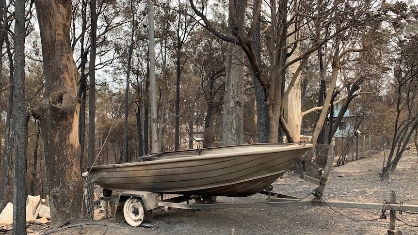 A burnt out boat sits in front of a destroyed home at Conjola Park on the South Coast.