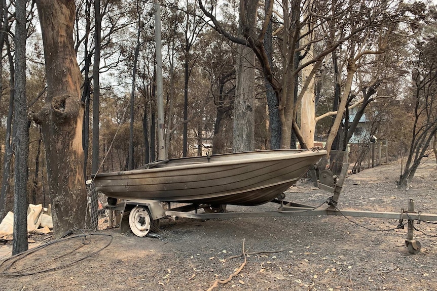 A burnt out boat sits in front of a destroyed home at Conjola Park on the South Coast.