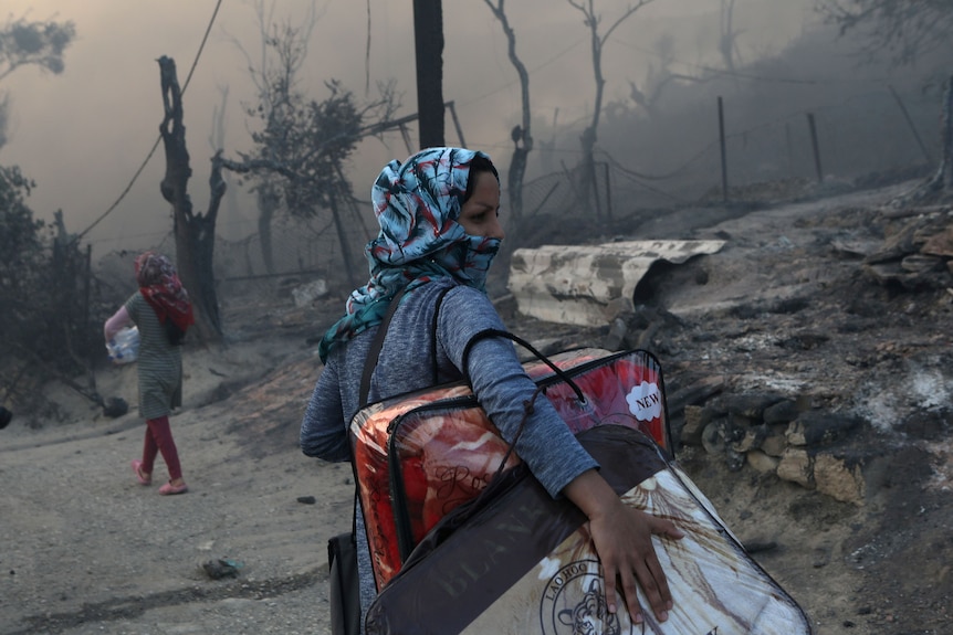 A woman carries her belonging in front of a burnt out landscape.
