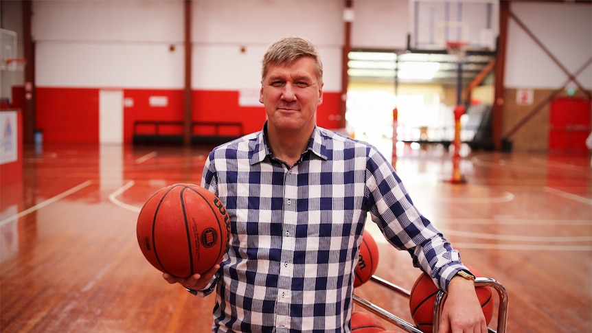 Paul Bartlett stands on an indoor basketball court holding a basketball.