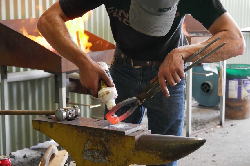 Man pouring powder on a molten horseshoe resting on an anvil.