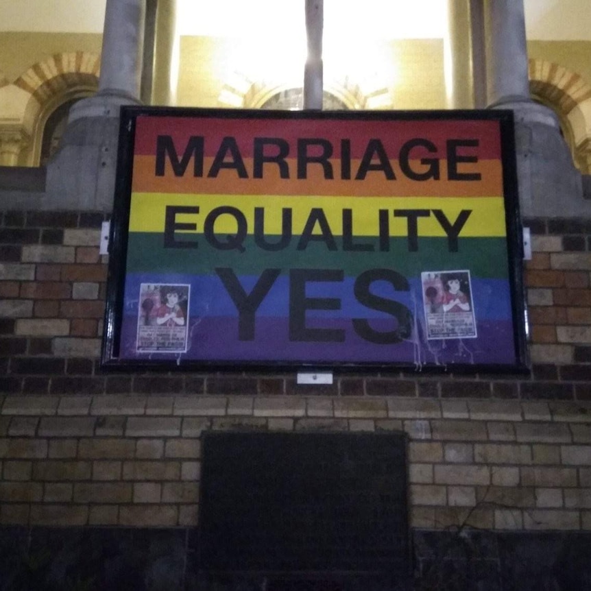 Two small anti same-sex marriage poster glued to the top of a rainbow flag saying 'Marriage Equality Yes'.