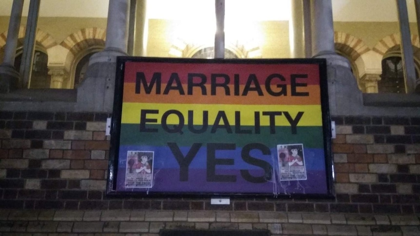 Two small anti same-sex marriage poster glued to the top of a rainbow flag saying 'Marriage Equality Yes'.