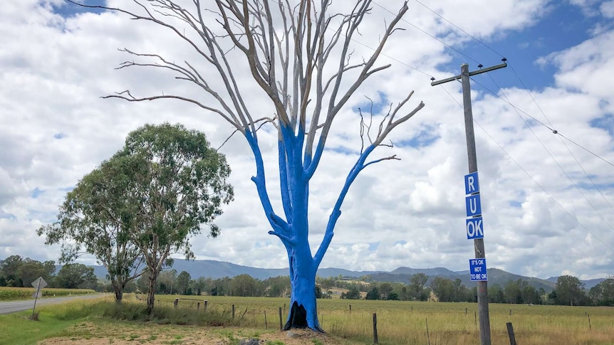 A tree painted blue with three people standing nearby.