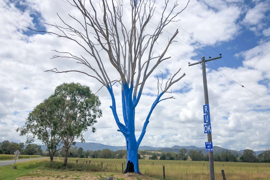 A tree painted blue with three people standing nearby.