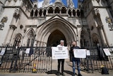 Two men with signs stand outside court building.