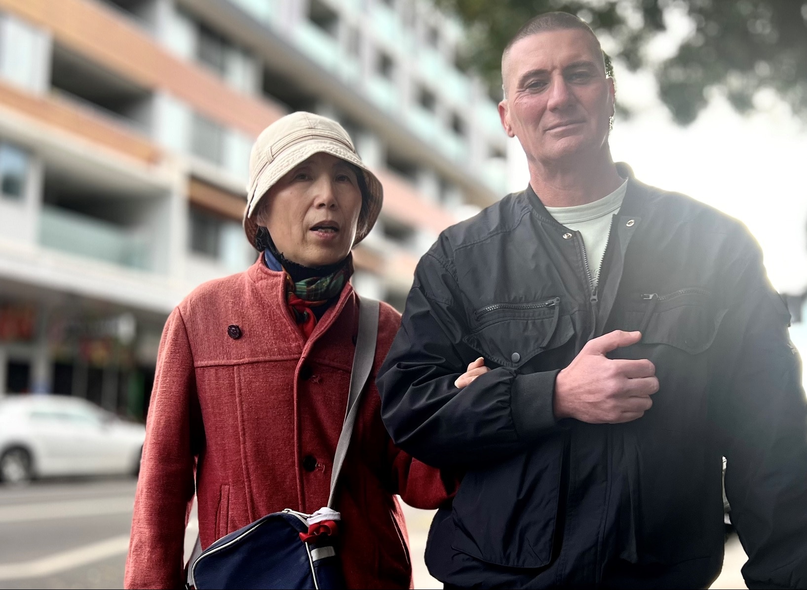 An elderly Asian woman standing next to a larger, middle-aged Caucasian male.