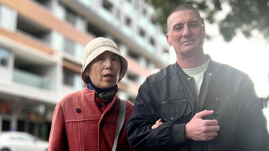 An elderly Asian woman standing next to a larger, middle-aged Caucasian male.