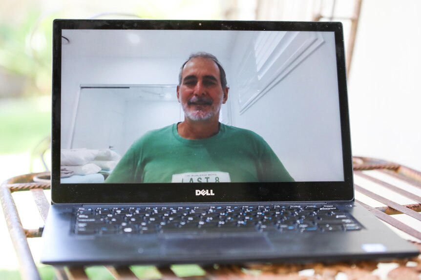 A man in a green shirt smiling on a laptop screen.