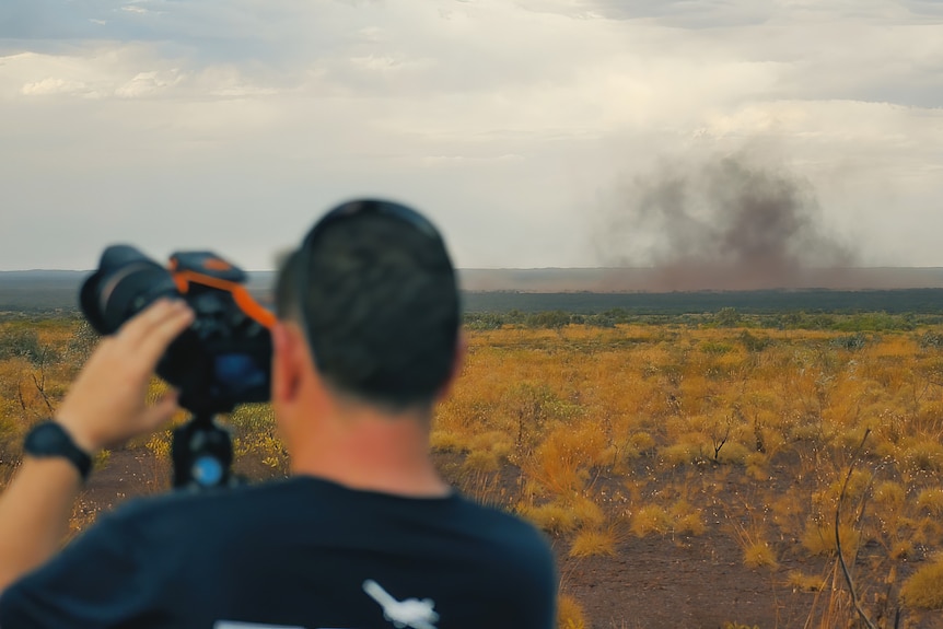 Jordan is holding his camera while a small dust storm forms in the distance