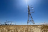 Picture from the ground looking up at a high-voltage transmission tower, with wind turbines in the background