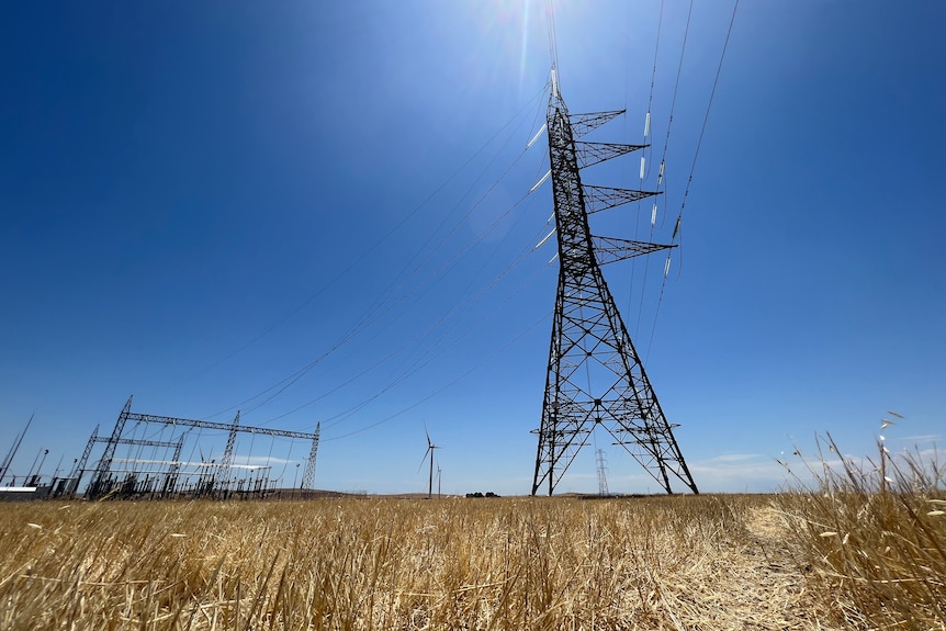 Picture from the ground looking up at a high-voltage transmission tower, with wind turbines in the background