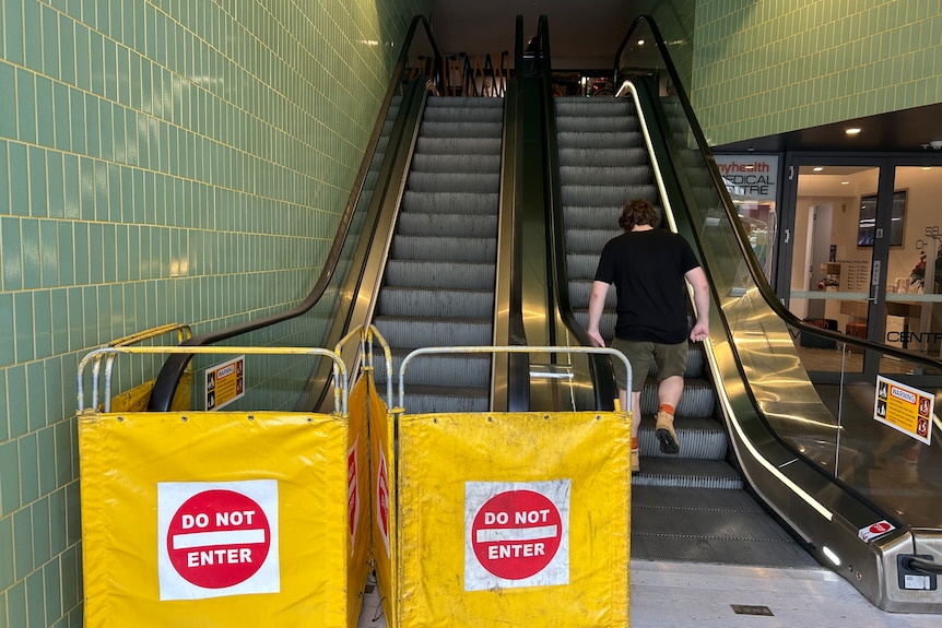Yellow 'Do not enter' signs at the base of an escalator leading to a supermarket.