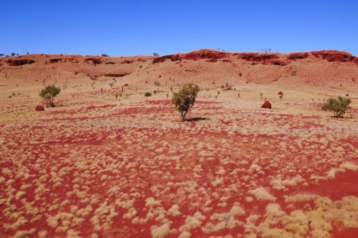 Dry landscape shows bushes, shrubs among dry hills with a blue sky.