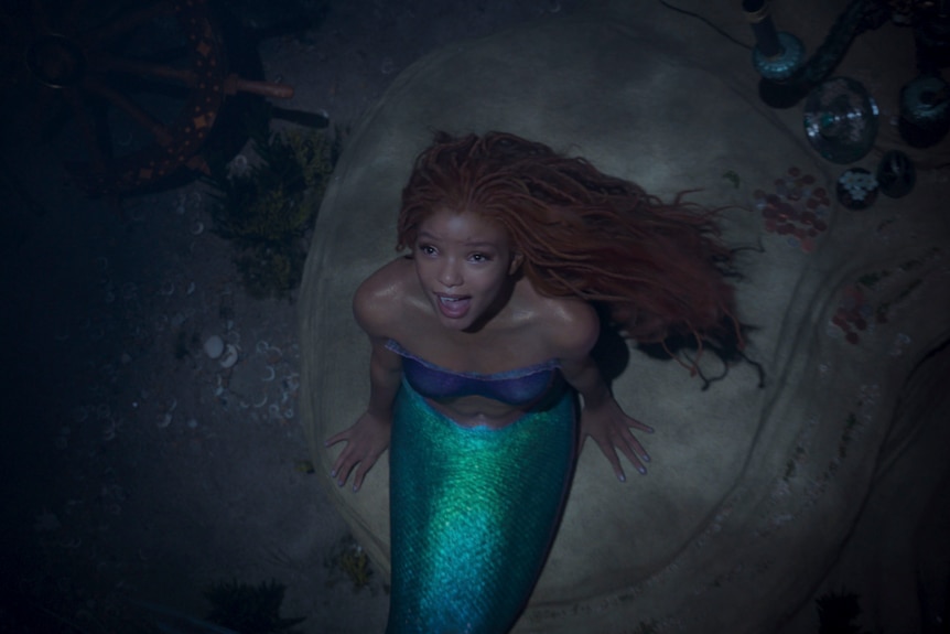 Halle Bailey singing as Ariel in The Little Mermaid. She has long red dreads and a fish tail.