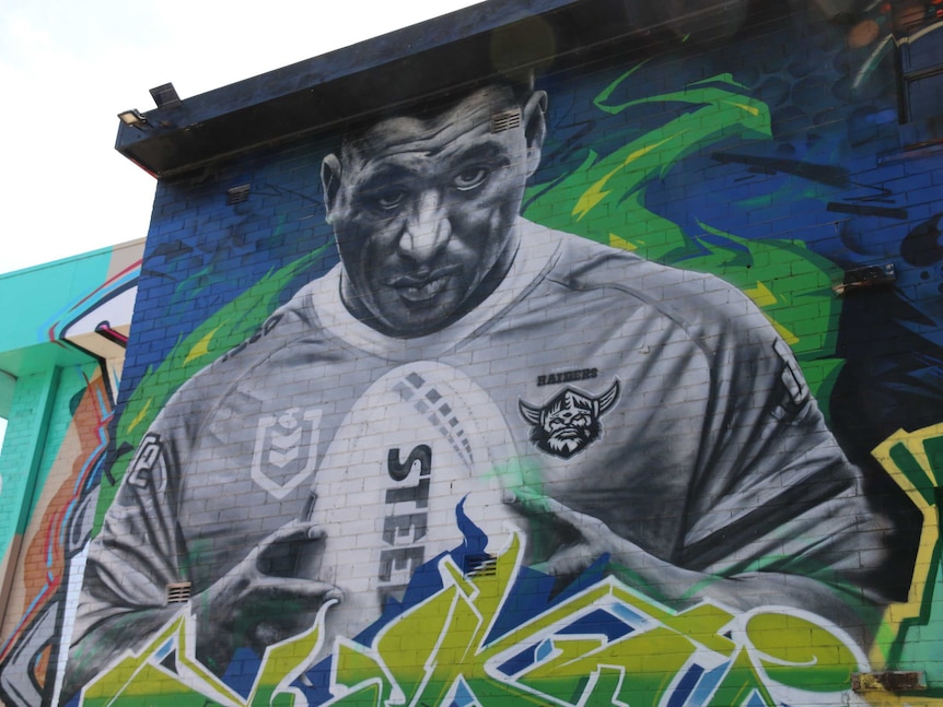 Papalii holds a football and looks serious in the black and white mural on the wall.