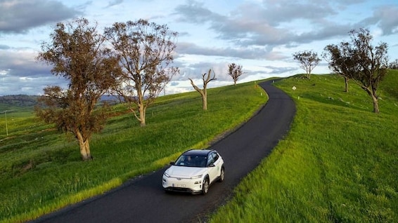 An electric car drives through green countryside.