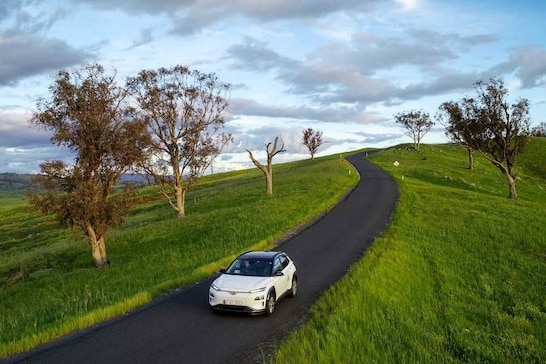 An electric car drives through green countryside.