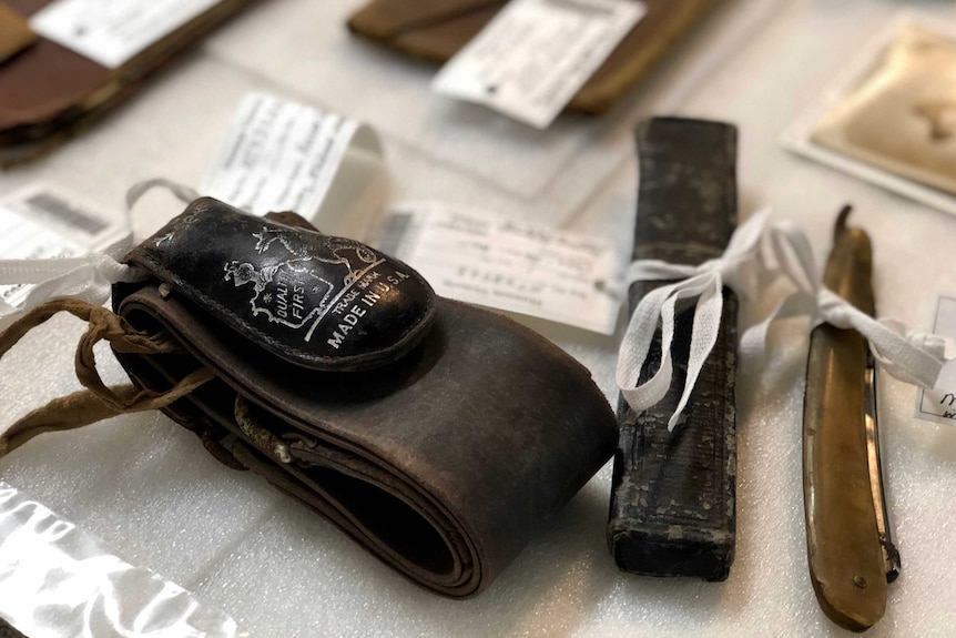 Old items from a WWI soldier's suitcase laid out on a table and labelled with white cards.