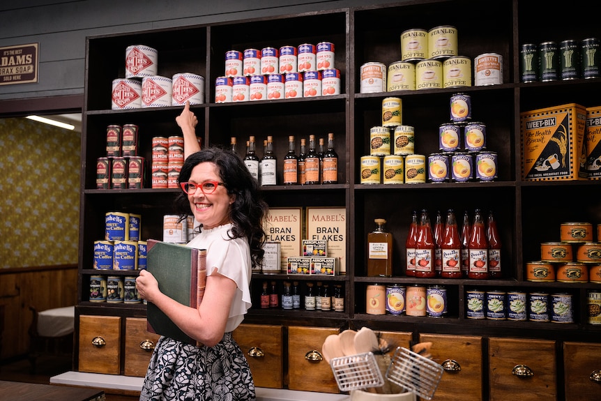 Woman pointing to a shelf with cans of food with old fashioned labels.