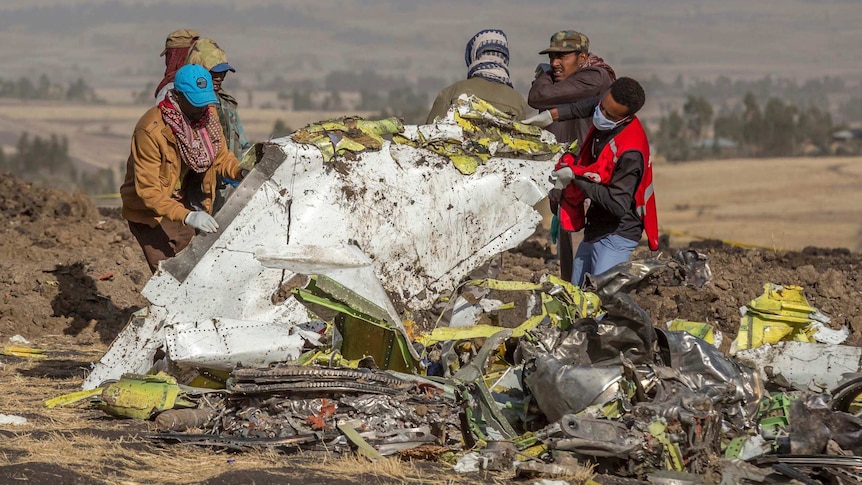 Men wearing masks and headwear lift up wreckage of an aircraft in Ethiopia.