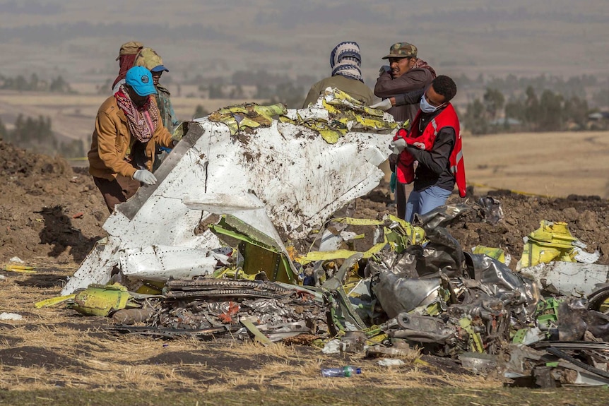 Men wearing masks and headwear lift up wreckage of an aircraft in Ethiopia.