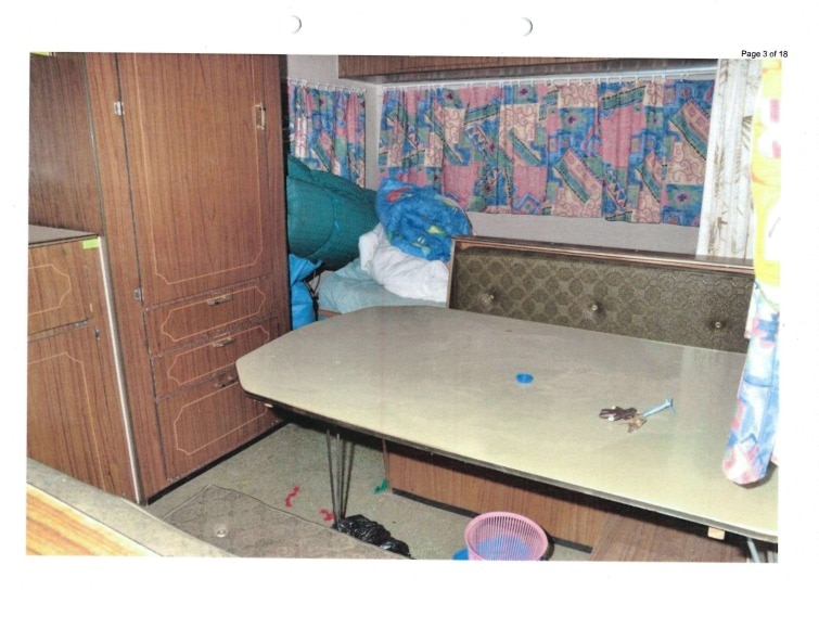 The interior of a caravan. shows a dinner table with a bench seat and a bed in the corner.