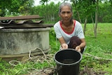 A woman crouching next to a well, tipping a bucket of brown water