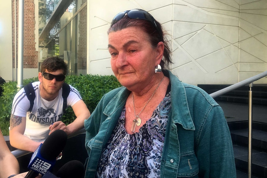 A woman in a denim jacket speaks to journalists on the steps outside the Perth District Court.