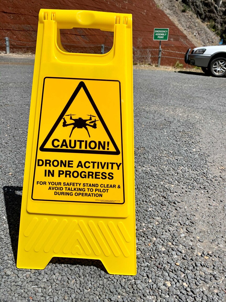 A yellow caution sign with a picture of a drone in black.
