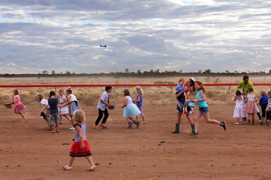 The kids collect lollies off the race track while the mustering plane circles overhead.