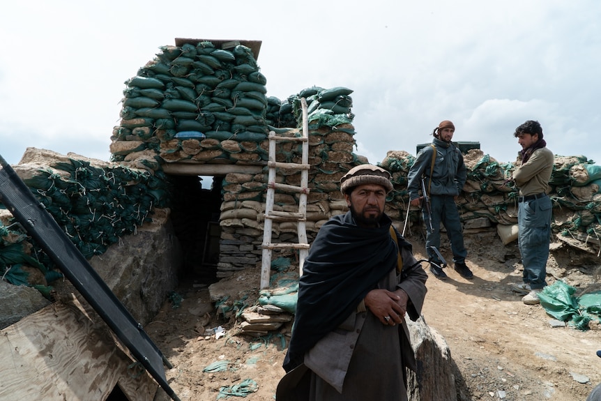 A man crouches in front of a checkpoint built from piles of sandbags