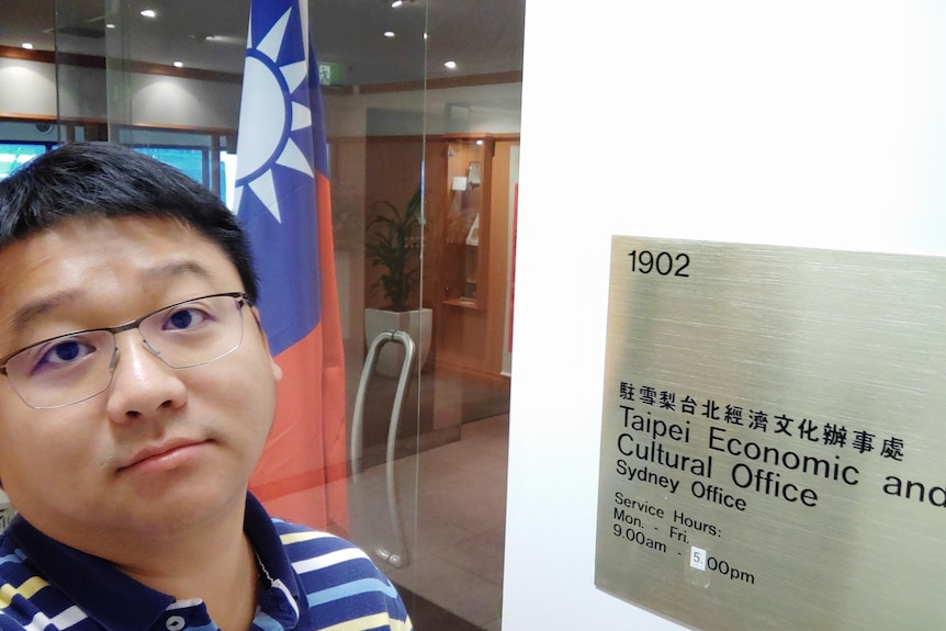 Peter Huang poses for a photo next to a sign that reads "Taipei Economic and Cultural Office".