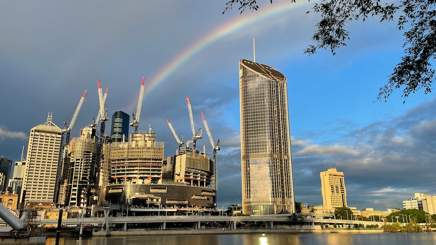 looking across Brisbane River from South Bank as sun reflects off buildings and a rainbow in the sky.