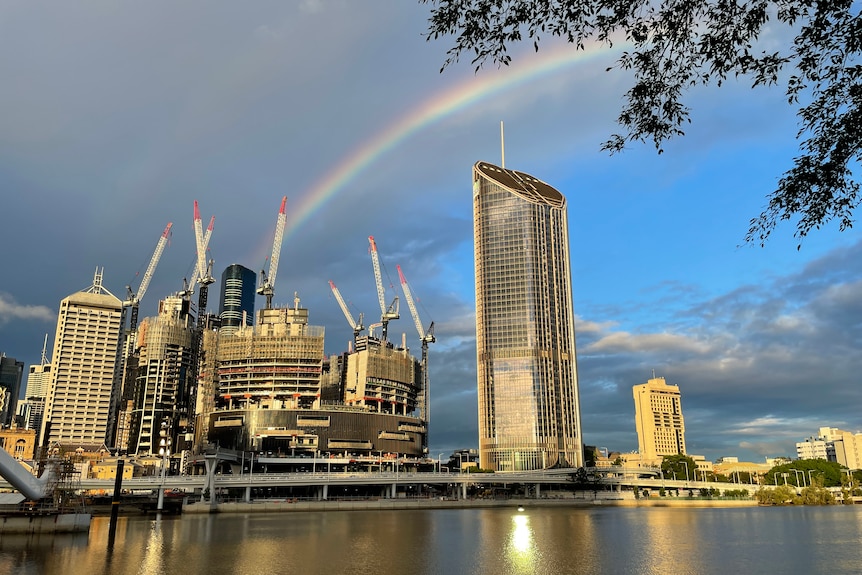 looking across Brisbane River from South Bank as sun reflects off buildings and a rainbow in the sky.