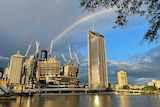 looking across Brisbane River from South Bank as sun reflects off buildings and a rainbow in the sky.